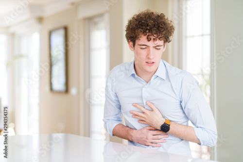 Young business man with curly read head with hand on stomach because indigestion, painful illness feeling unwell. Ache concept.