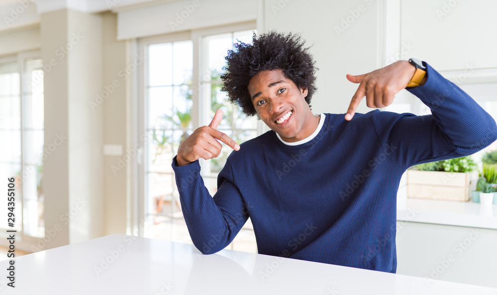 Young african american man wearing casual sweater sitting at home looking confident with smile on face, pointing oneself with fingers proud and happy.