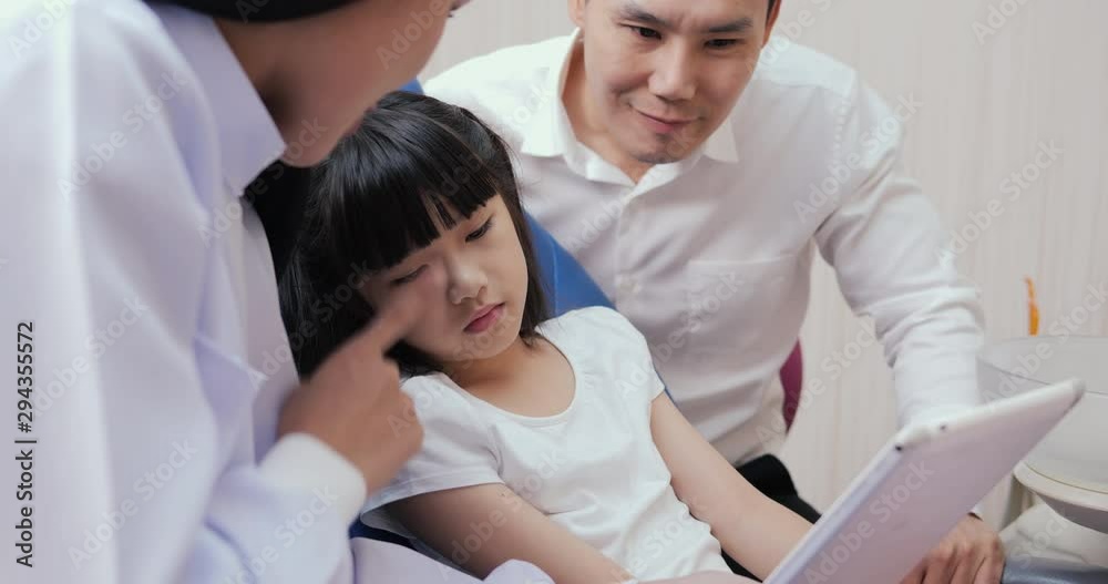 Little girl visiting doctor at dental clinic. Doctor and assistance showing information in tablet to child. Dental care concept. Little girl visiting doctor at dental clinic. Doctor and assistance showing information in tablet to child. Dental care concept.