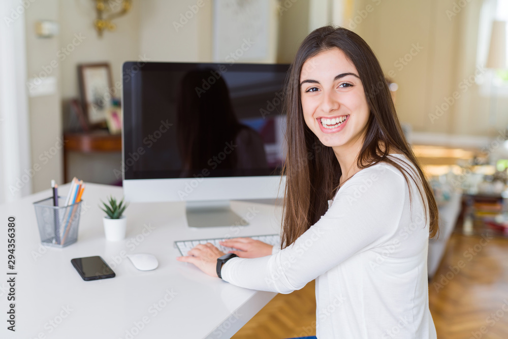 Young woman smiling working using computer and showing a blank screen on the background Young woman smiling working using computer and showing a blank screen on the background
