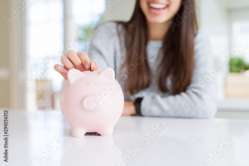 Young woman smiling putting a coin inside piggy bank as savings for investment