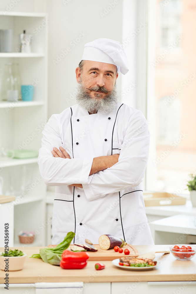 Waist up portrait of cheerful senior chef looking at camera standing with arms crossed in restaurant kitchen Waist up portrait of cheerful senior chef looking at camera standing with arms crossed in restaurant kitchen