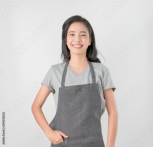 Tela Asian woman in apron and standing and looking forward on gray background