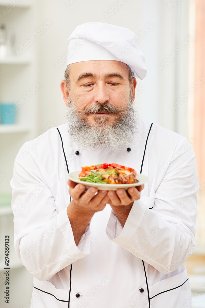 Portrait of bearded senior chef holding delicious meat steak while standing in restaurant kitchen, copy space Portrait of bearded senior chef holding delicious meat steak while standing in restaurant kitchen, copy space