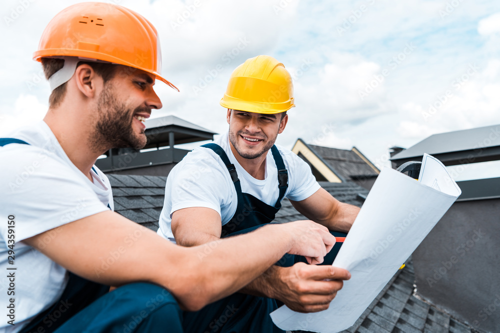 selective focus of happy builder looking at coworker and holding blueprint selective focus of happy builder looking at coworker and holding blueprint