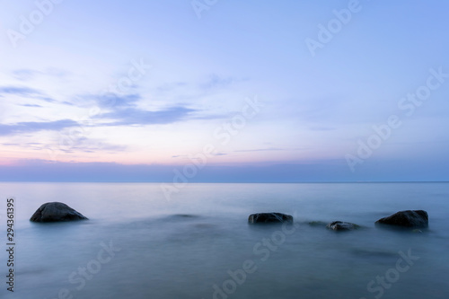 long exposure smooth sea surface with large rocks sticking out of the water in twilight blue light