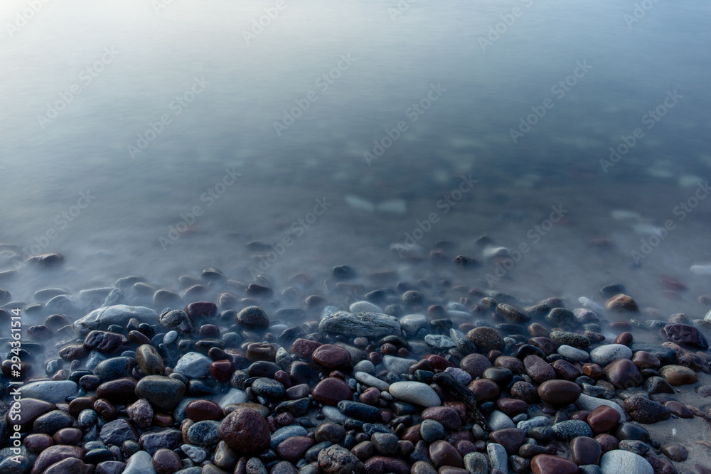 multi-colored smooth stones by the sea at a long exposure in twilight - obrazy, fototapety, plakaty 