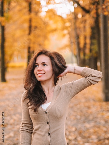 Brunette girl with long hair stands on the background of Golden autumn landscape, beautiful colorful trees