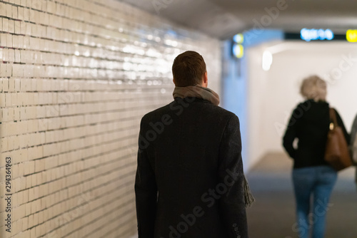 Man in overcoat following a woman in subway