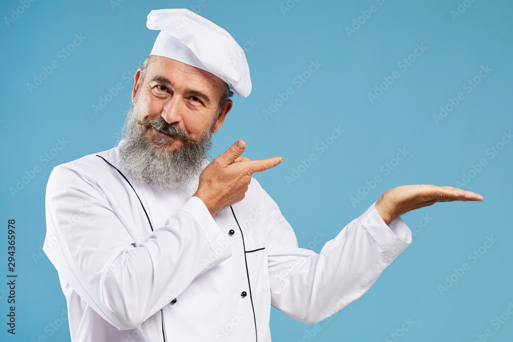Waist up portrait of charismatic bearded chef pointing at copy space standing against blue background, mock up template Waist up portrait of charismatic bearded chef pointing at copy space standing against blue background, mock up template