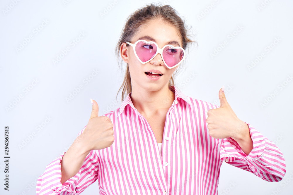 Cool Kazakh girl stylishly dressed in pink joyfully shows thumbs up on a white background