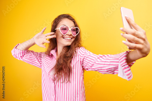 Young funny blogger Asian girlmakes selfie on the phone camera on yellow background, isolated in studio