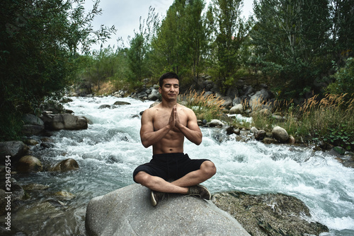 Kazakh muscular athlete man trains and exercises by the river in nature. Asian handsome does extreme fitness workout outdoors