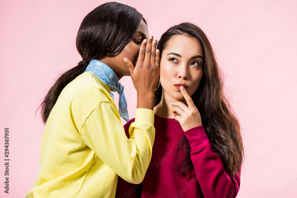 african american woman telling secret to her asian friend isolated on pink african american woman telling secret to her asian friend isolated on pink