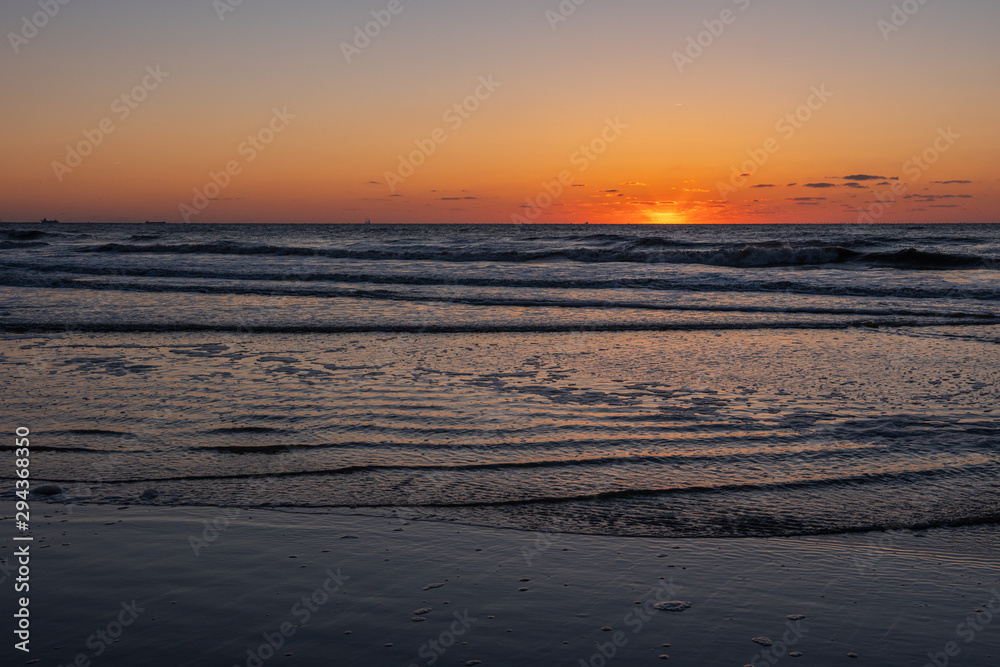 Amazing sunset view on the beach. Beautiful sunset landscape at the North sea and orange sky above it with awesome sun golden reflection on waves as a background.