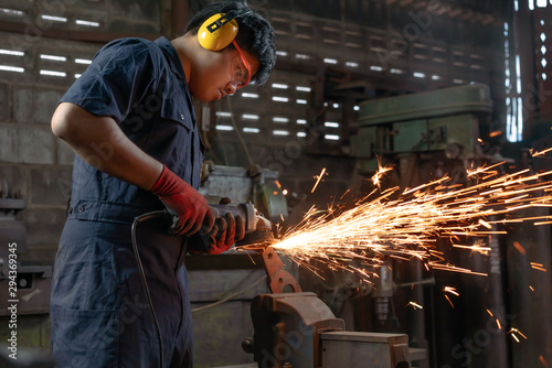Diverse Asian male engineer operating power tools with sparks in industrial factory
