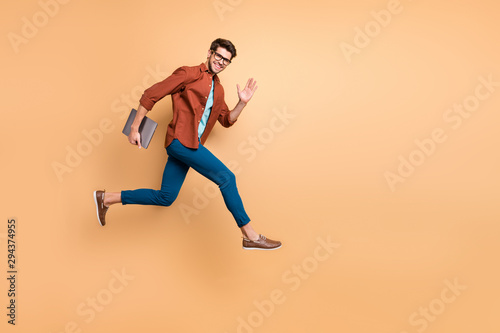 Full length body size view of his he nice attractive cheerful cheery glad content guy jumping in air carrying laptop running fast late hurry-up meeting isolated over beige color pastel background