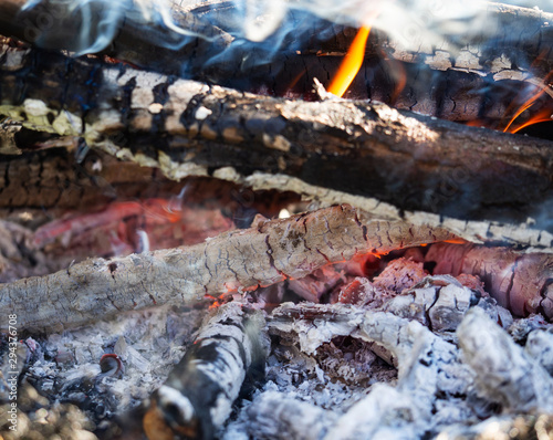 Glowing embers in the ash with log in smoke, closeup