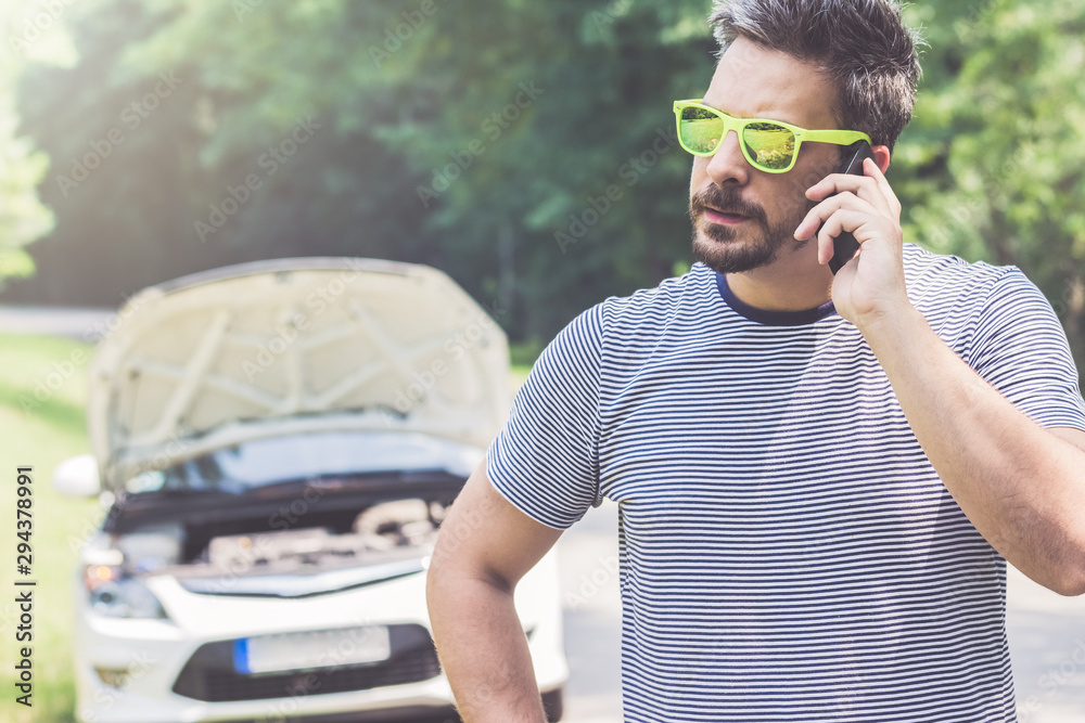 Fototapeta premium Man talking on mobile phone and broken car in the background