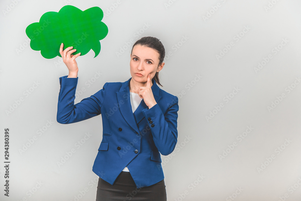 Attractive teacher holding a green speech bubble, keeping finger on the cheek, thinking, looking seriously at the camera.