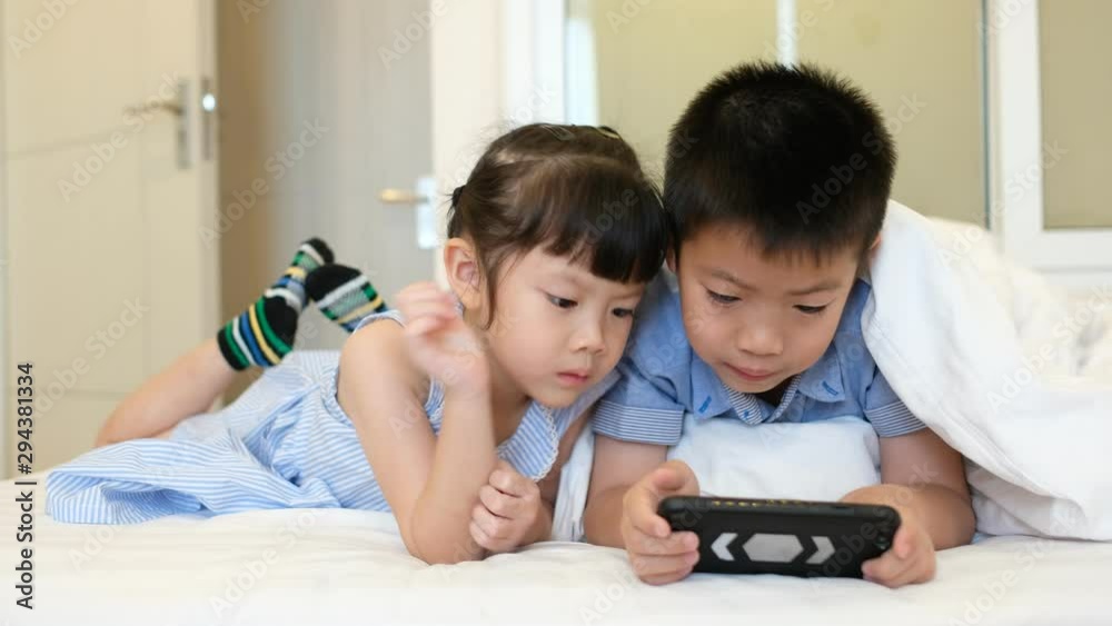 two chinese children addicted tablet, asian child watching tablet, kid use telephone together on their bed, play phone, kid addict smartphone