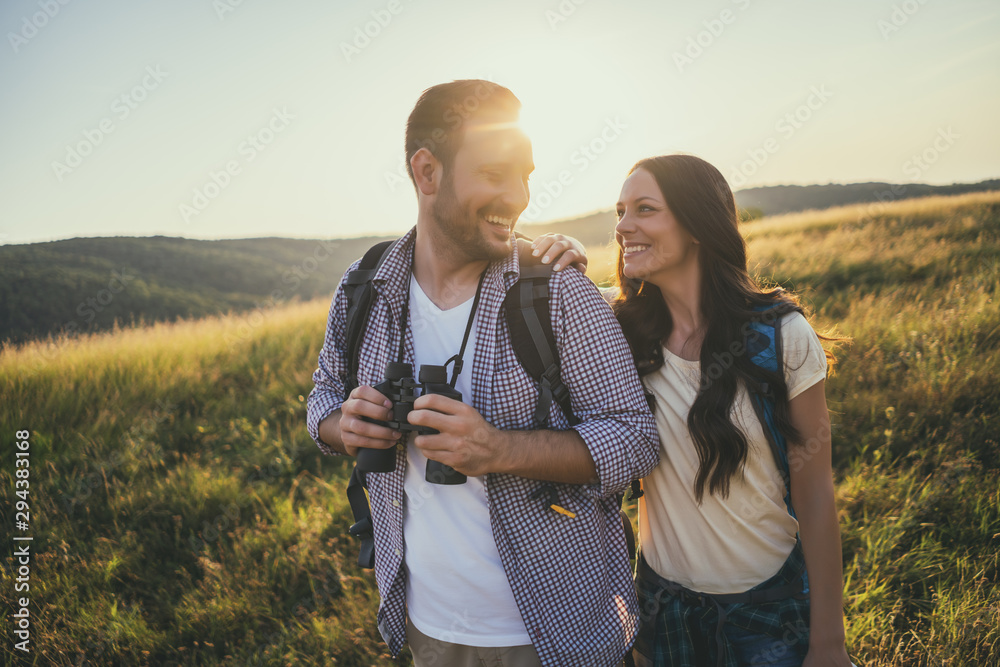 Happy couple is hiking in mountain. They are watching nature with binoculars. - obrazy, fototapety, plakaty 