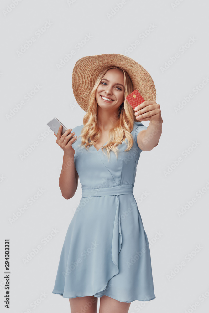 Attractive young woman smiling and showing credit card while standing against grey background Attractive young woman smiling and showing credit card while standing against grey background