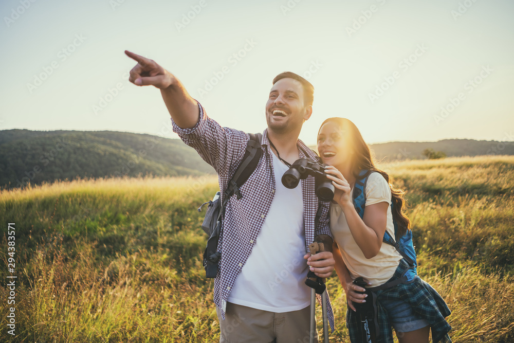 Happy couple is hiking in mountain. They are watching nature with binoculars. - obrazy, fototapety, plakaty 
