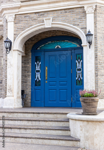 Modern entrance to the building  a ceramic pot with green heather. Large blue door. The entrance from the sidewalk to the building.