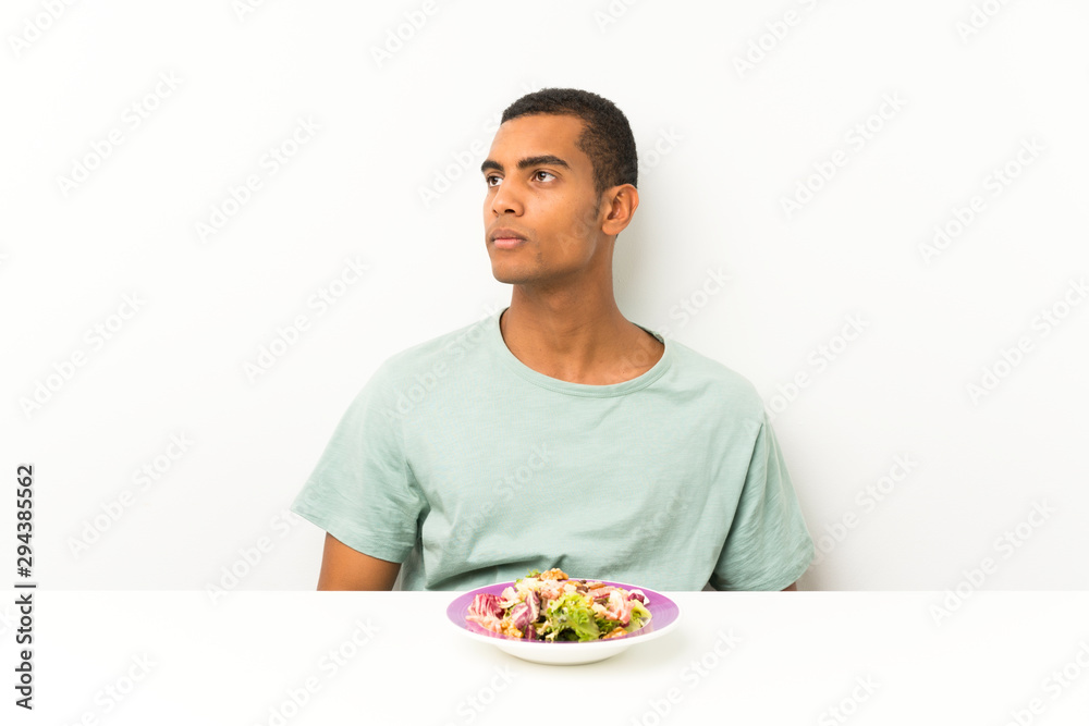 Young handsome man with salad in a table looking side Young handsome man with salad in a table looking side