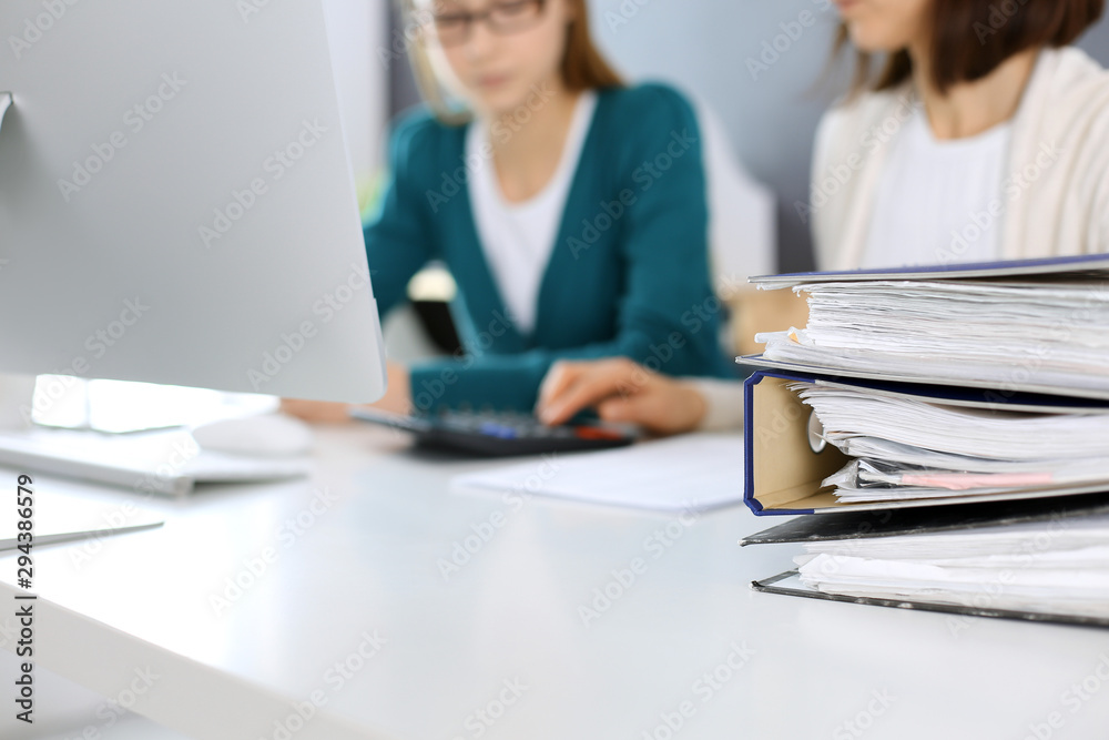Calculator and binders with papers are waiting to be processed by business woman or bookkeeper working at the desk in office back in blur. Internal Audit and tax concept Calculator and binders with papers are waiting to be processed by business woman or bookkeeper working at the desk in office back in blur. Internal Audit and tax concept