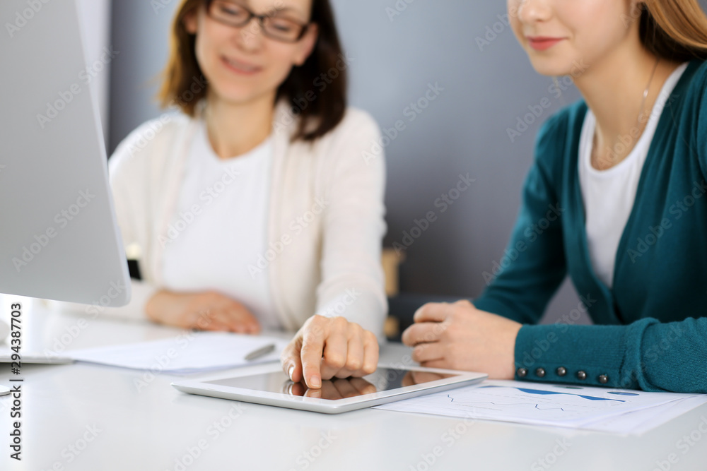Businesswoman pointing at tablet computer screen while giving presentation to her female colleague. Group of business people working at the desk in office. Teamwork concept Businesswoman pointing at tablet computer screen while giving presentation to her female colleague. Group of business people working at the desk in office. Teamwork concept