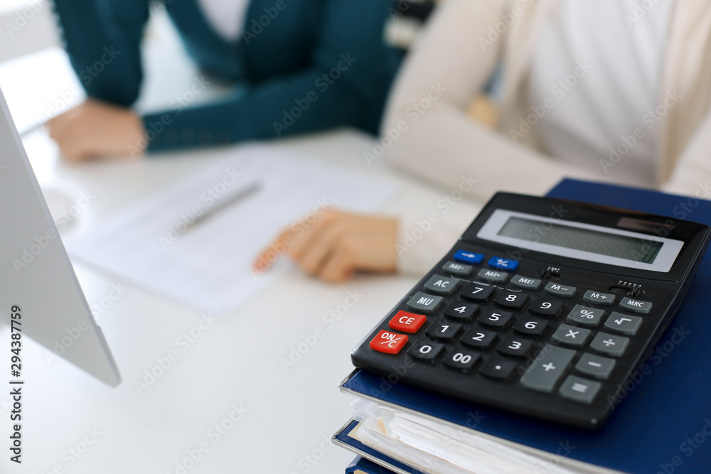 Calculator and binders with papers are waiting to be processed by business woman or bookkeeper working at the desk in office back in blur. Internal Audit and tax concept Calculator and binders with papers are waiting to be processed by business woman or bookkeeper working at the desk in office back in blur. Internal Audit and tax concept