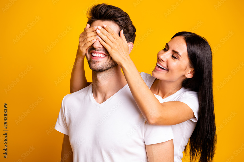 Guess who. Photo of amazing lady hiding eyes macho guy making unexpected surprise wear casual white t-shirts isolated yellow color background Guess who. Photo of amazing lady hiding eyes macho guy making unexpected surprise wear casual white t-shirts isolated yellow color background