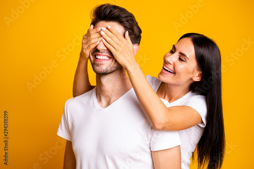 Guess who. Photo of amazing lady hiding eyes macho guy making unexpected surprise wear casual white t-shirts isolated yellow color background © deagreez