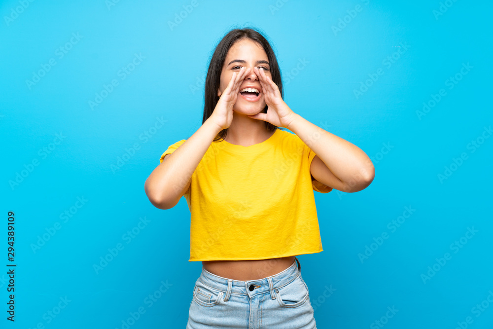 Young girl over isolated blue background shouting and announcing something