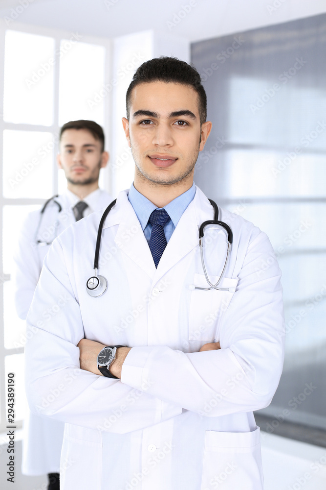 Arab doctor man standing with caucasian colleague in medical office or clinic. Diverse doctors team, medicine and healthcare concept