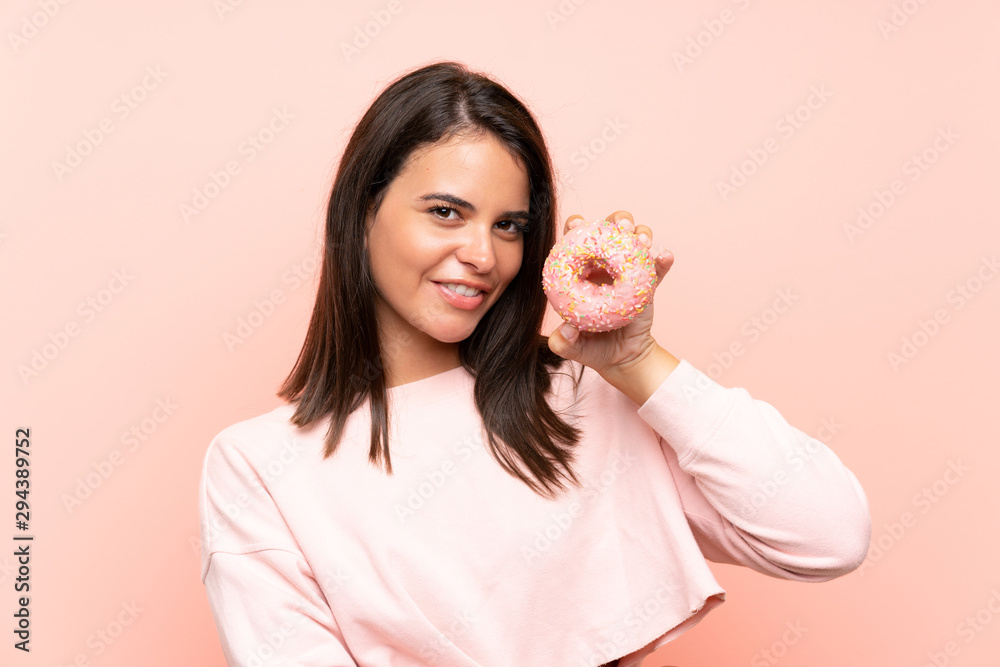 Young girl holding a donut over isolated pink background Young girl holding a donut over isolated pink background