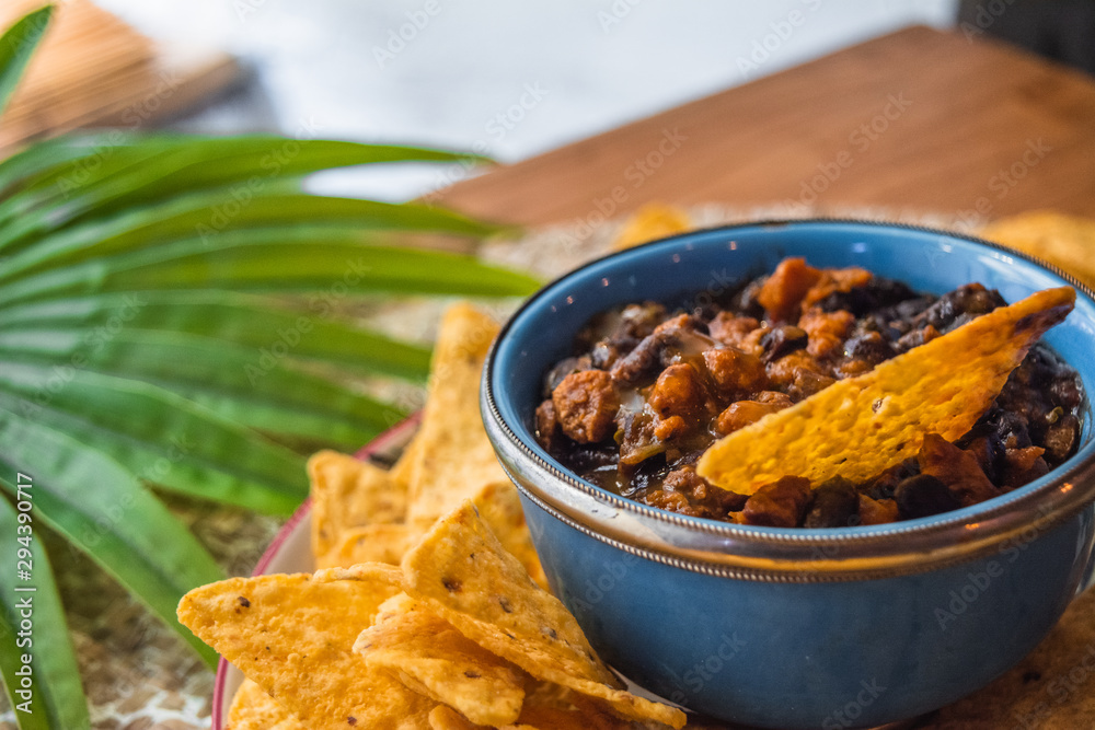 Fototapeta premium Bol azul con nachos, aluvias negras y una hoja de palma de fondo