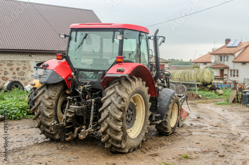 Red  tractor and agricultural equipment in the yard of a dairy farm. Back view. A barn and an apartment building in the background . Podlasie  Poland.