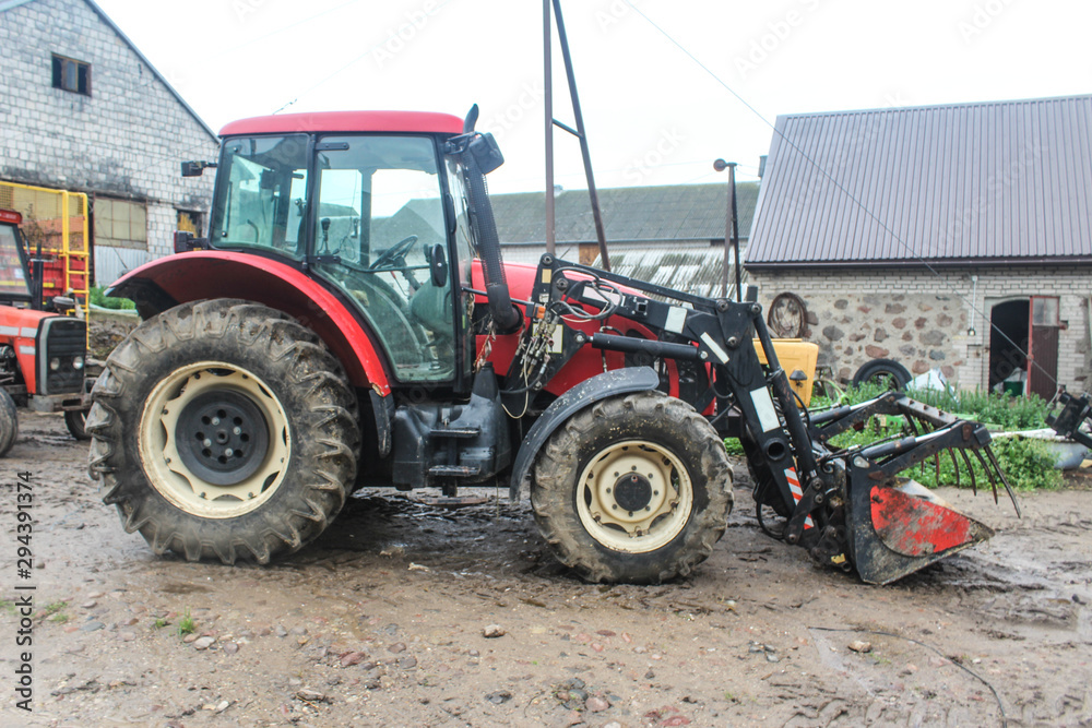 Red tractor with a lift for various works in the yard of a dairy farm. Side view. A barn in the background. Podlasie, Poland.