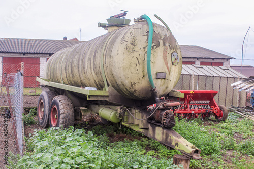 Tank for various liquids on a dairy farm. Barn and seeder in the background. .Side view. Podlasie, Poland.