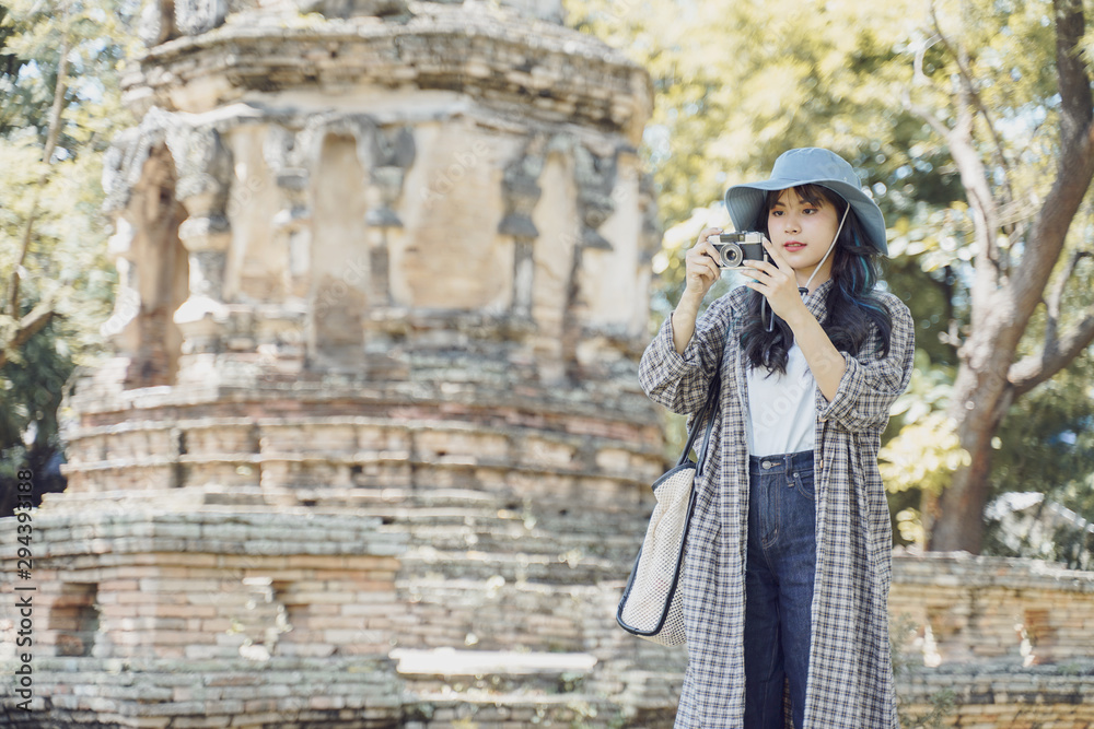 Young asian female traveler taking a photo with retro camera while traveling in popular tourist attraction thailand ancient temple.