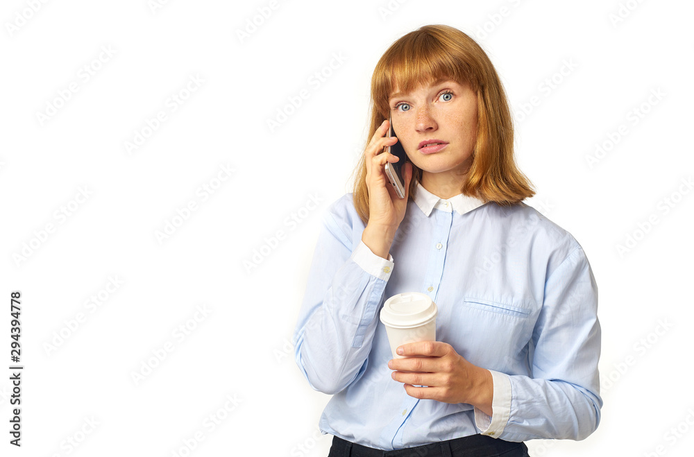 Portrait of young redheaded woman with freckles and bang talking on a phone looking worried and holding a cup of coffee in her hands Portrait of young redheaded woman with freckles and bang talking on a phone looking worried and holding a cup of coffee in her hands