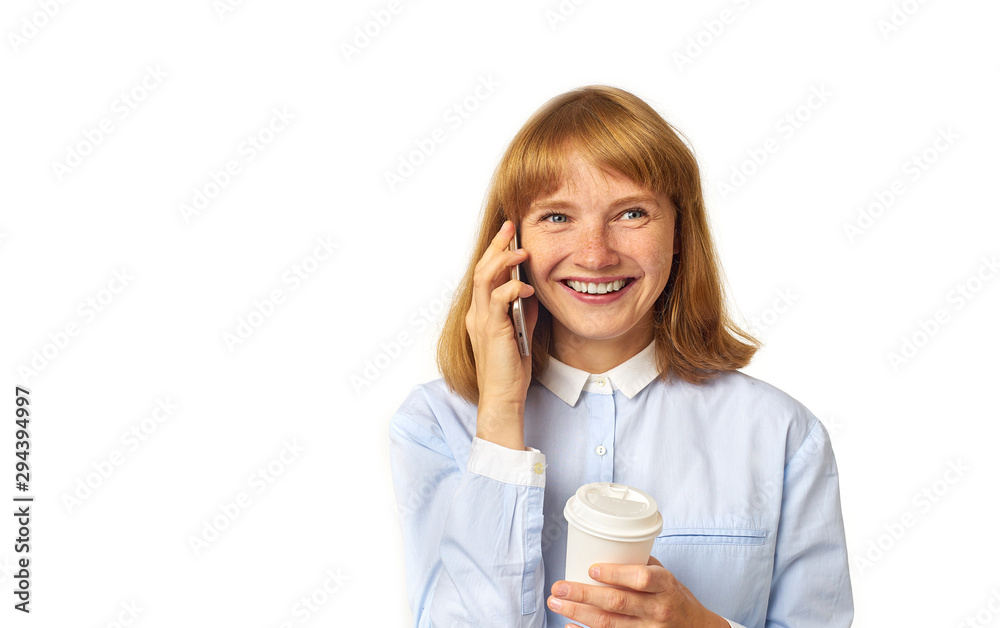 Portrait of young redheaded woman with freckles and bang talking on a phone smiling and holding a cup of coffee in her hands