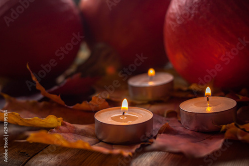 Composition with pumpkins and candles on maple leaves on wooden background. Side view. Selective soft focus.