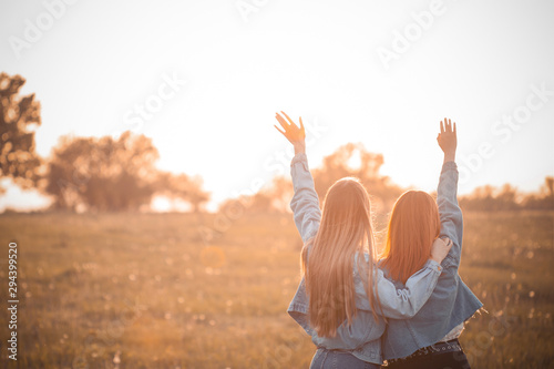 Two young women looking on the sunset and rise up hands. Best friends.