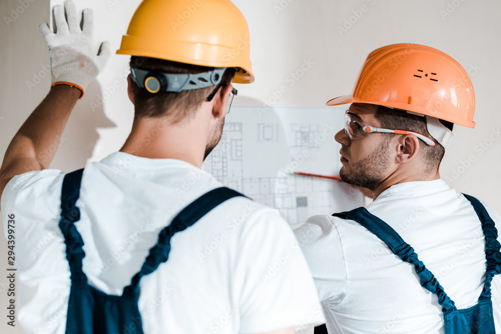 selective focus of architect in helmet looking at blueprint near coworker selective focus of architect in helmet looking at blueprint near coworker