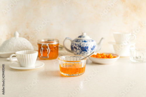 Buck seathorn jam, white tea cups with saucers, tea pot all set for breakfast with pastel colored table and wall photo