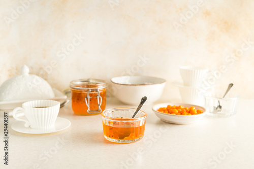 Buck seathorn jam in glass jars, white tea cups with saucers, bowls all set for breakfast with pastel colored table and wall
